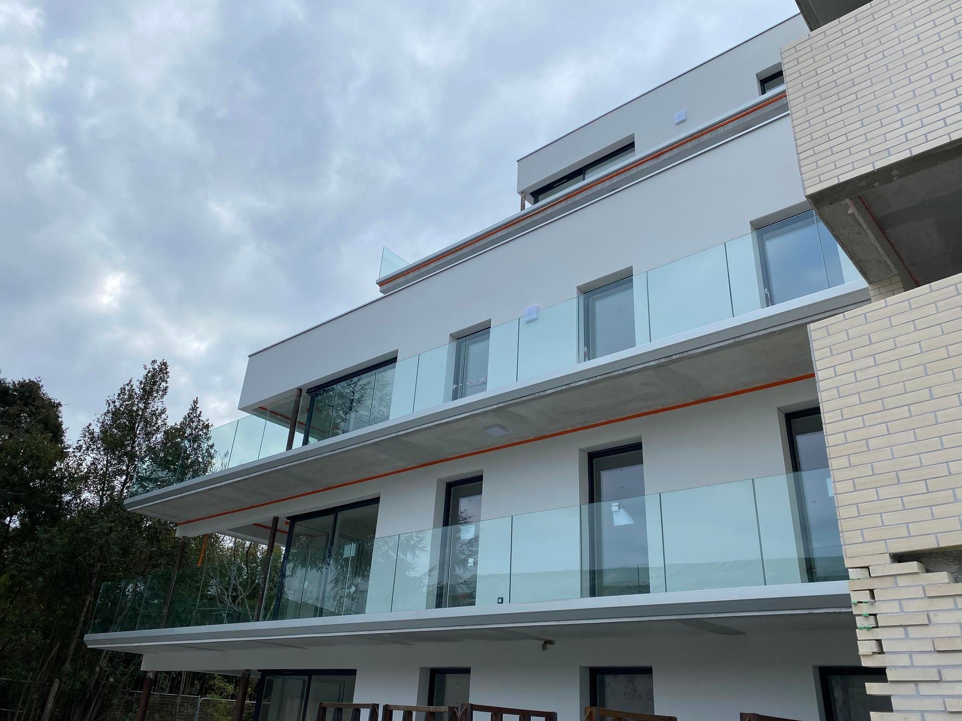 Vue en contre-plongée d'un immeuble d'appartements modernes blancs à plusieurs étages, avec des balustrades de balcon en verre et de grandes fenêtres.