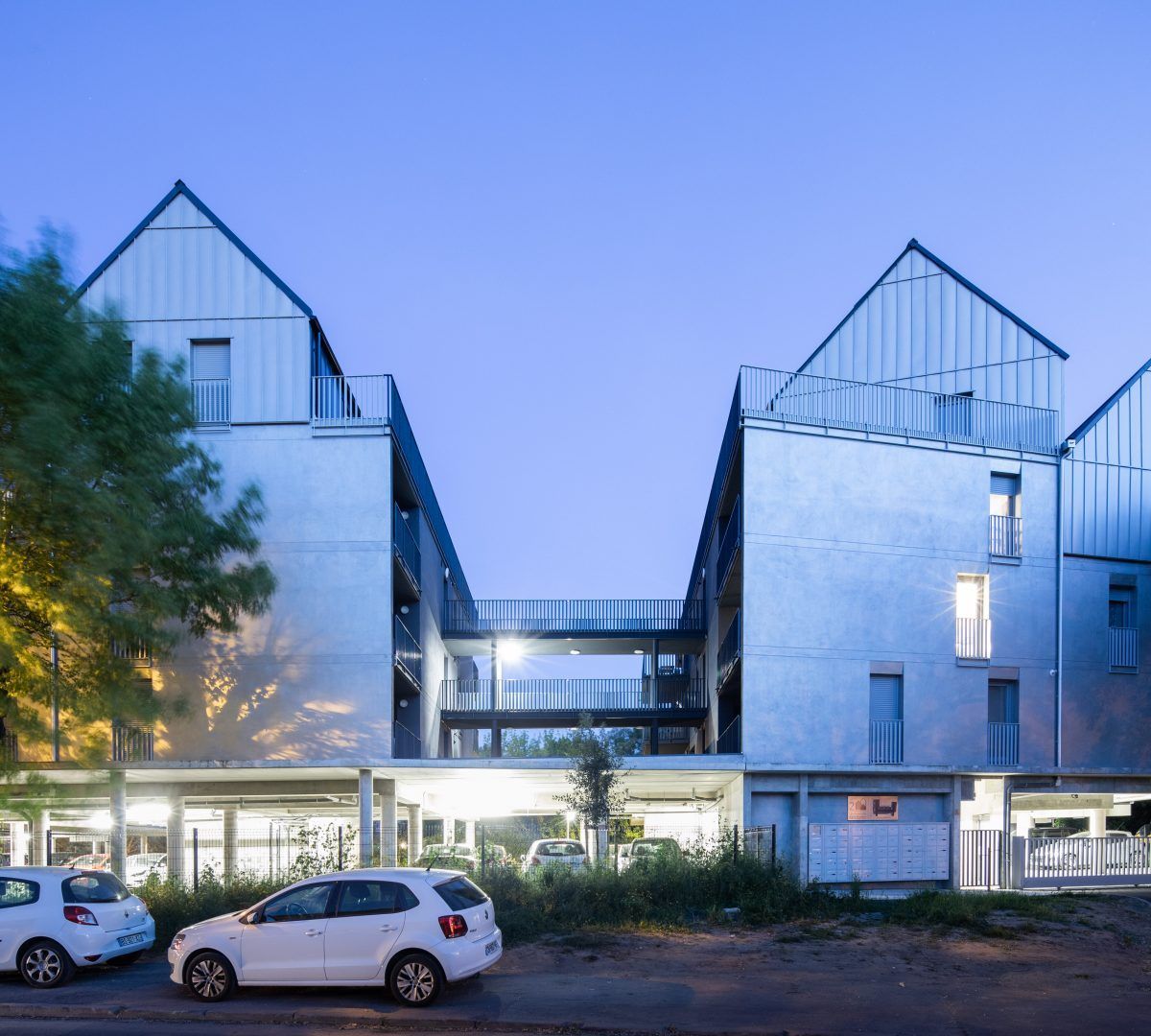 Immeubles d'appartements modernes en verre au crépuscule, voitures garées et fenêtres éclairées