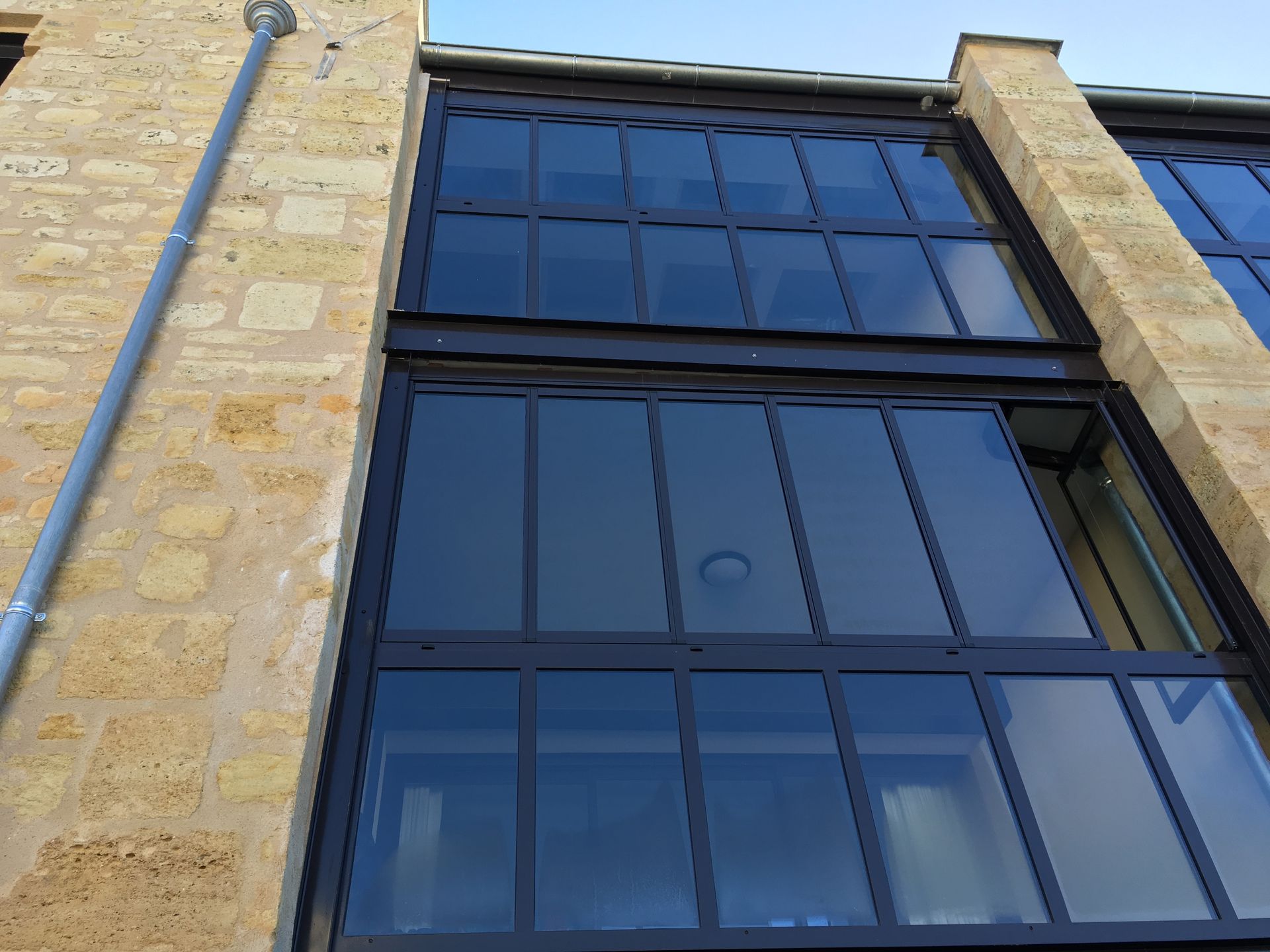 Une main agrippe une poignée de porte sombre et moderne, tirant pour ouvrir une fenêtre ou une porte donnant sur un espace vert extérieur.