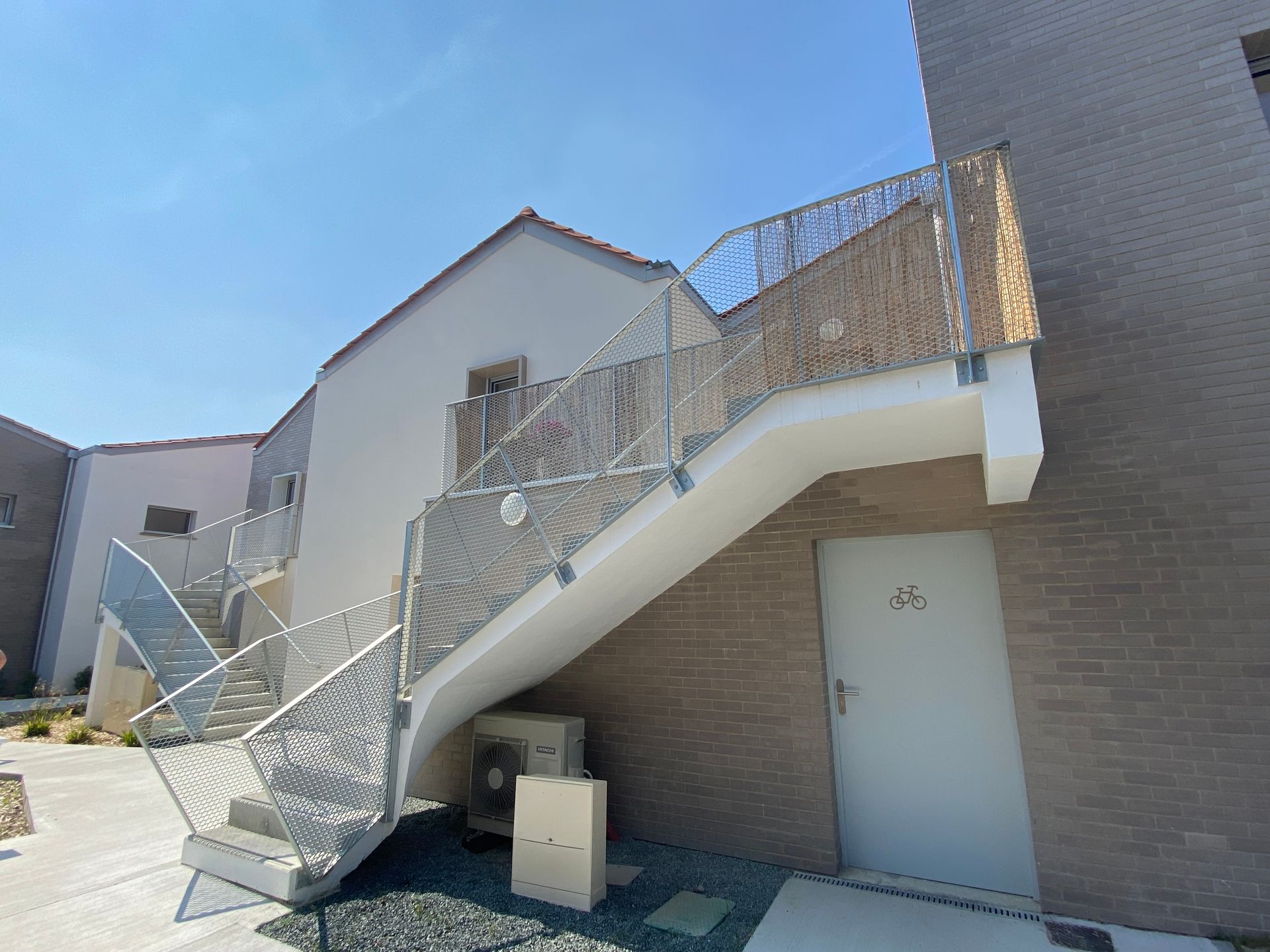 Escalier extérieur avec rampes métalliques menant à la porte d'un appartement à l'étage d'un immeuble en briques