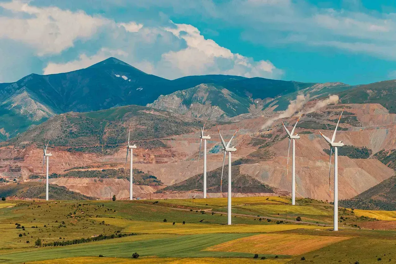Una hilera de turbinas eólicas en un campo con montañas al fondo.