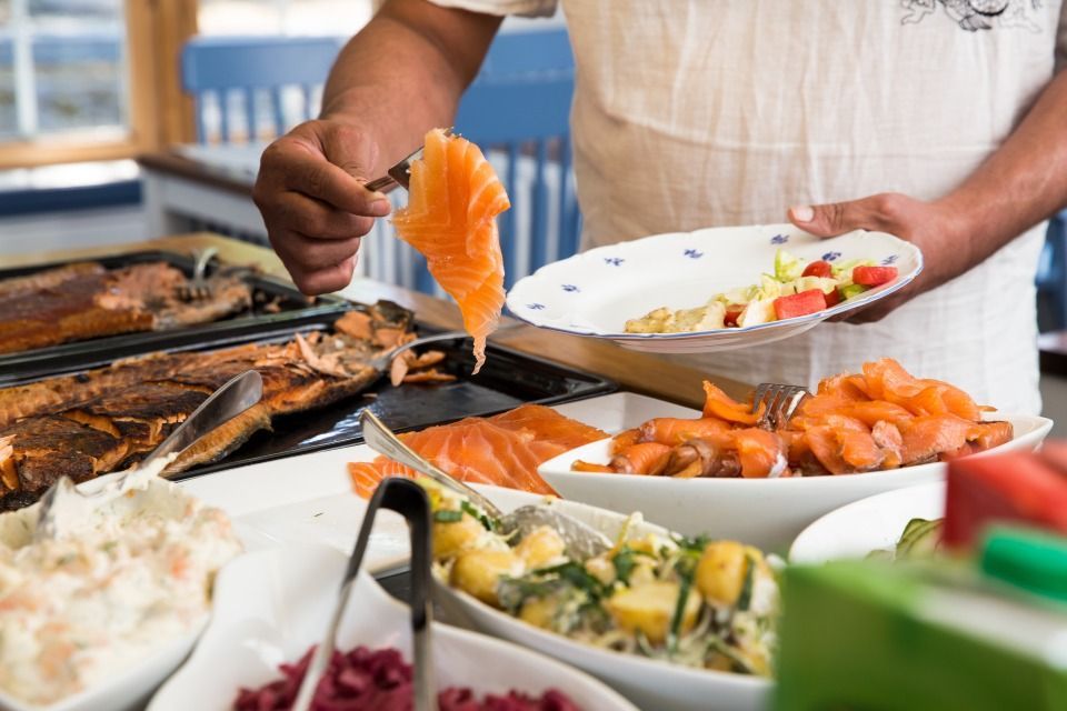 Man serving salmon from a buffet onto a plate with salad, in a restaurant.
