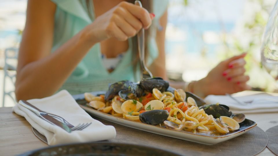 Woman eating pasta with mussels outdoors.