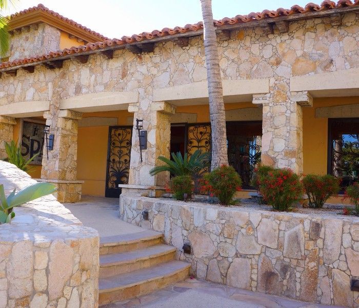 Outdoor lounge area overlooking a turquoise ocean. Sandy beach, sun loungers, seating, and water bottle.