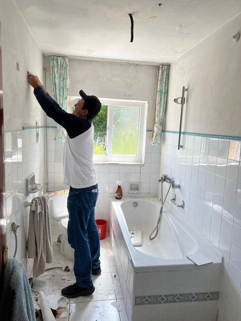 Un hombre está pintando una pared en un baño al lado de una bañera.