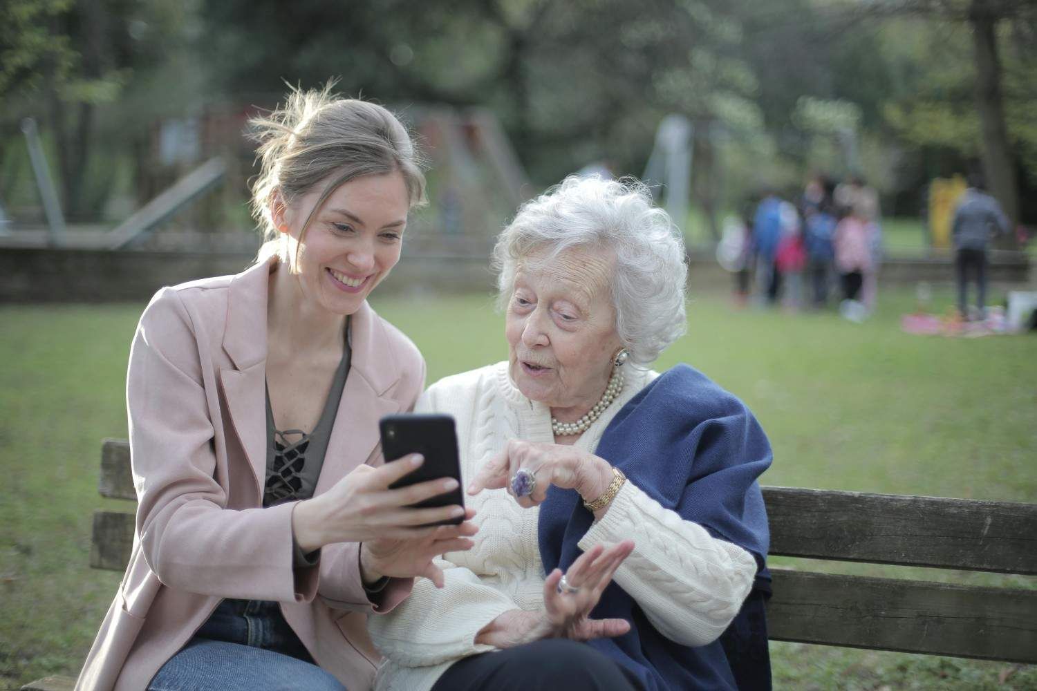 Una mujer muestra su teléfono a una persona mayor en un banco del parque, ambos sonriendo.