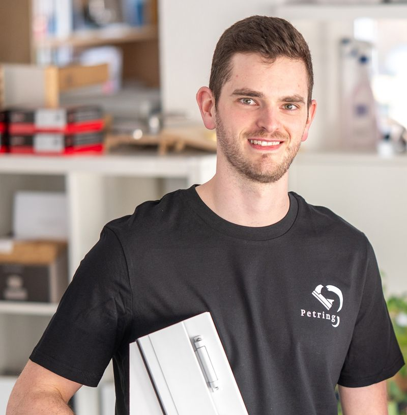 Lächelnder Mann im schwarzen T-Shirt hält im Haus einen Holzgegenstand, möglicherweise eine Pfeife.