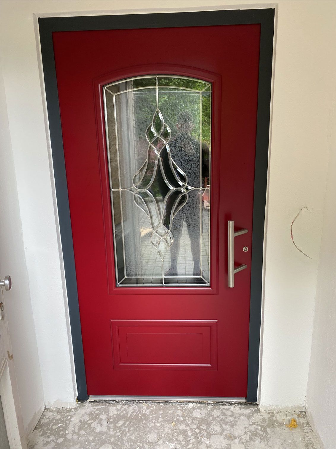 An einer weißen Wand steht eine rote Tür mit einem Buntglasfenster.