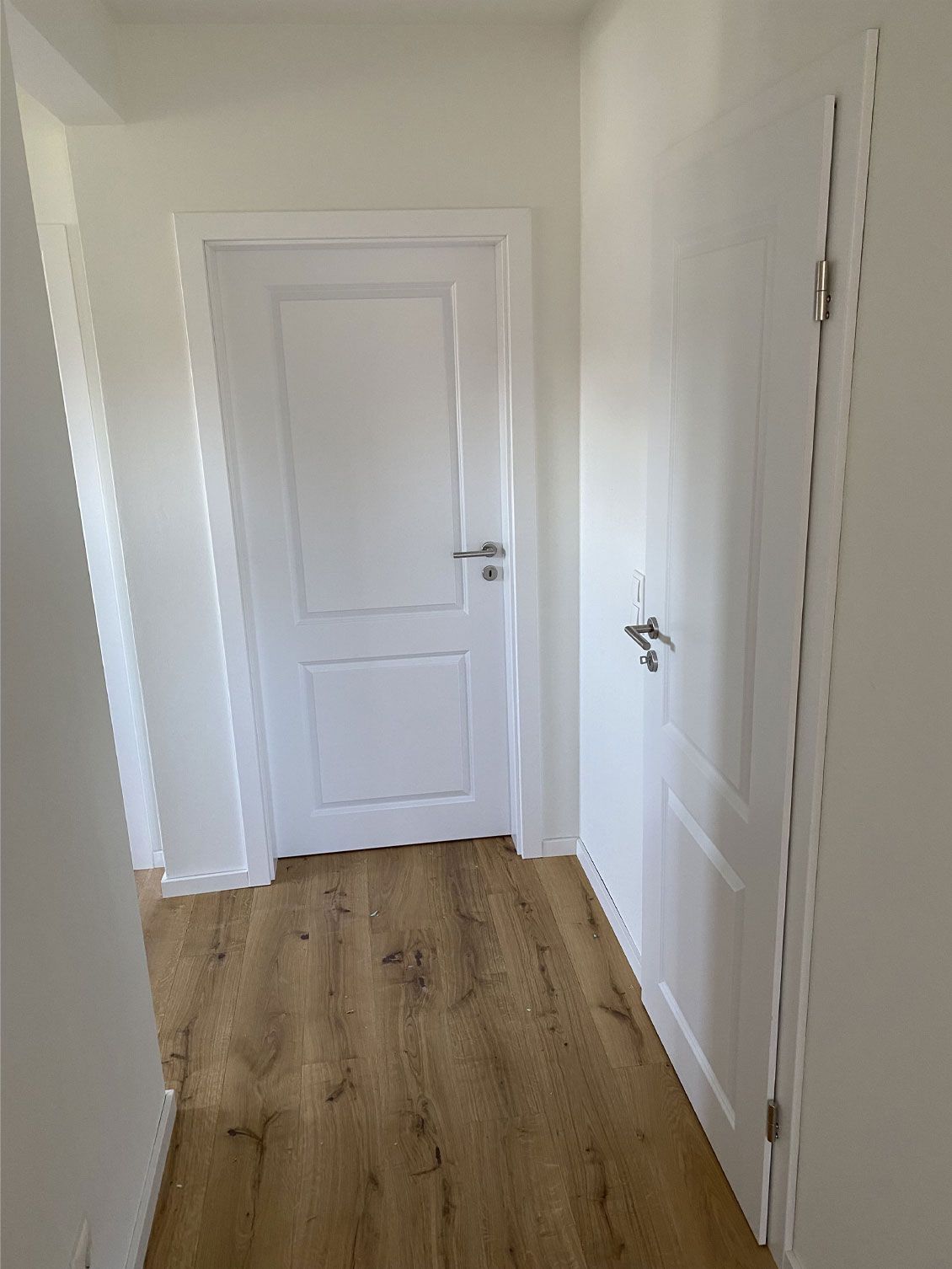 Ein Flur mit weißer Tür und Holzboden.