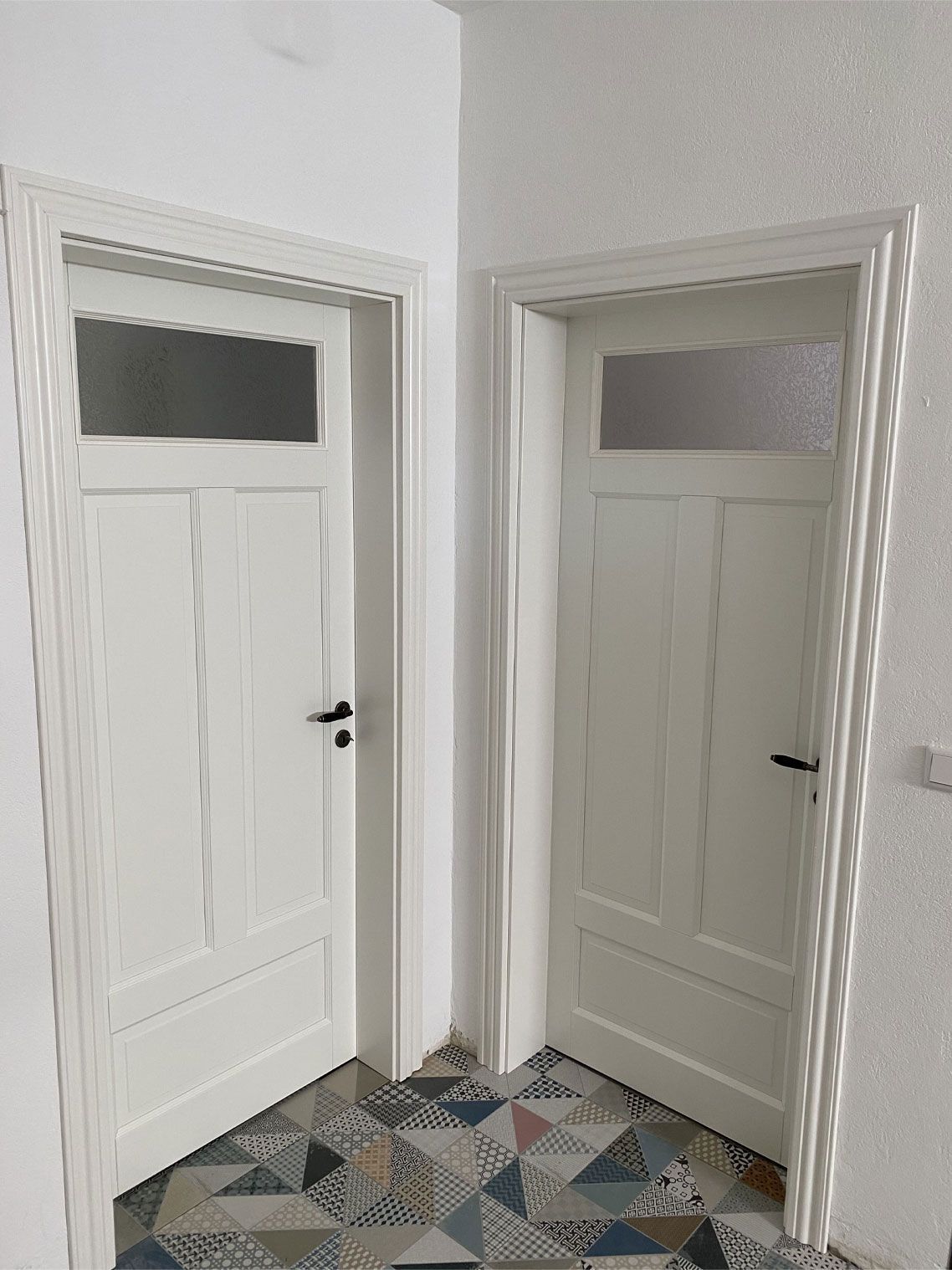 Ein Flur mit zwei weißen Türen und einem gefliesten Boden.