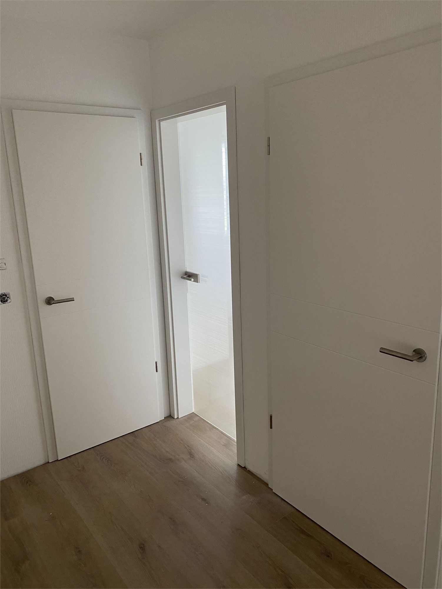 Ein Flur mit weißen Türen und Holzböden, der zu einem Badezimmer führt.