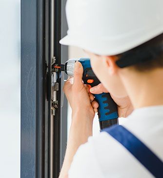 Ein Mann mit Schutzhelm repariert mit einer Bohrmaschine ein Fenster.