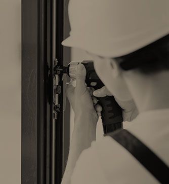 Ein Mann mit Schutzhelm arbeitet mit einem Schraubenzieher an einem Fenster.