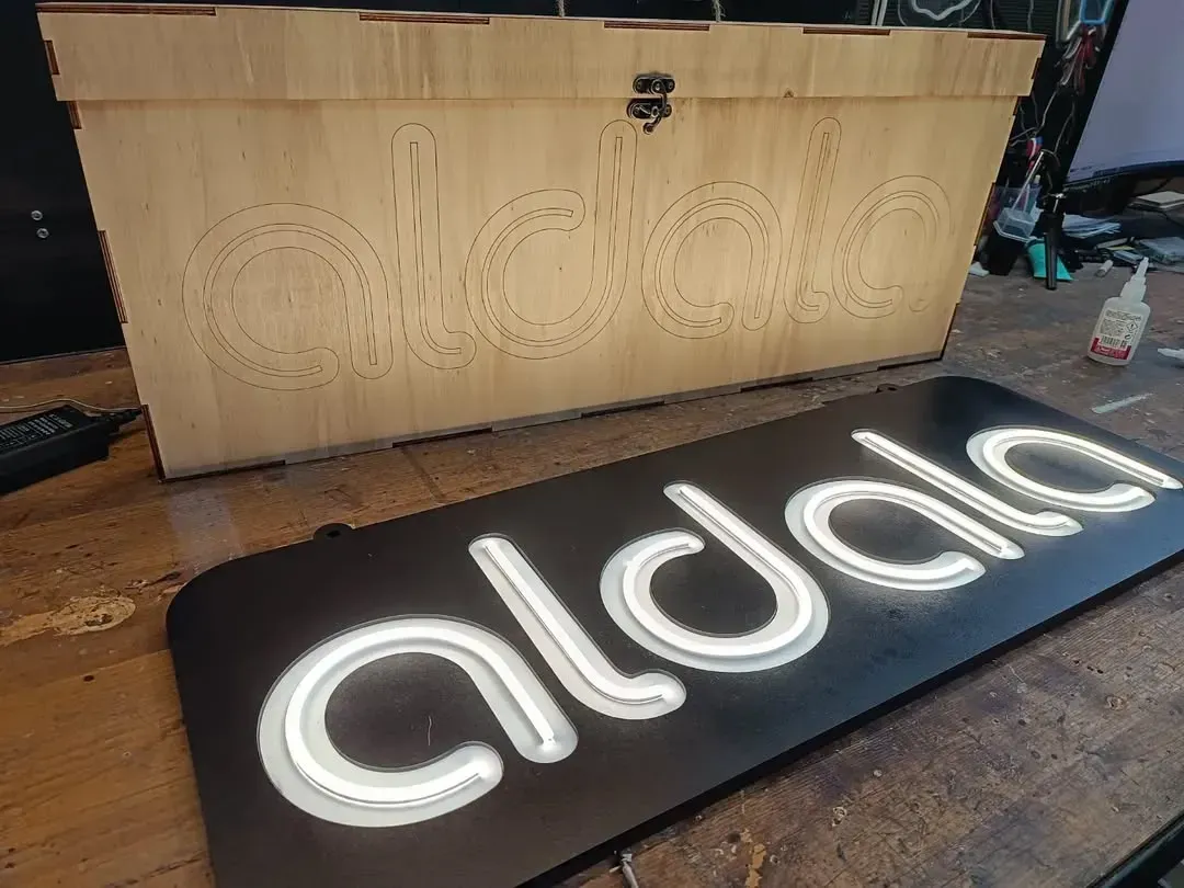 Un letrero de neón está sobre una mesa de madera al lado de una caja de madera.