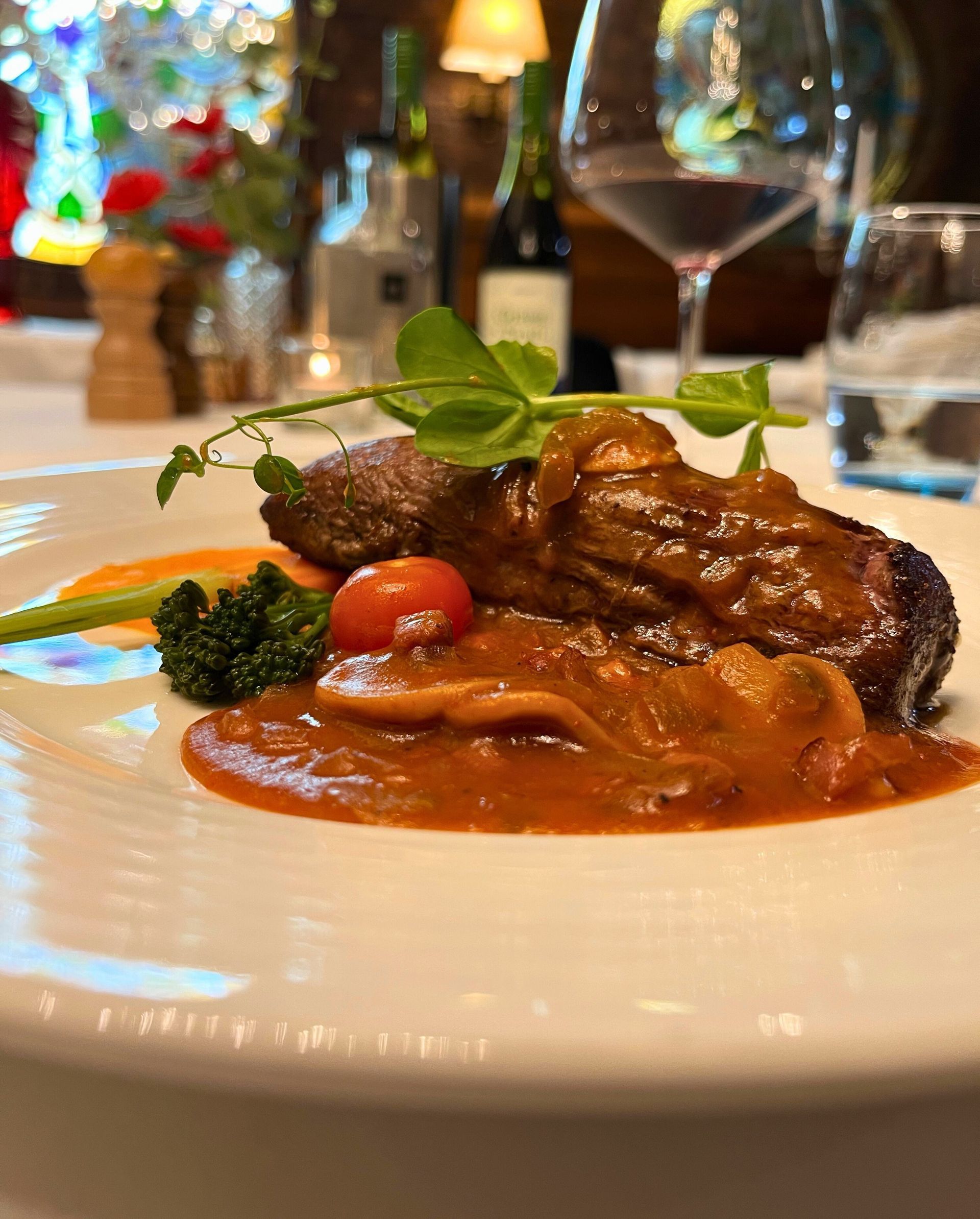 Steak mit Soße, Gemüse und einer Kirschtomate auf einem weißen Teller in einem Restaurant.
