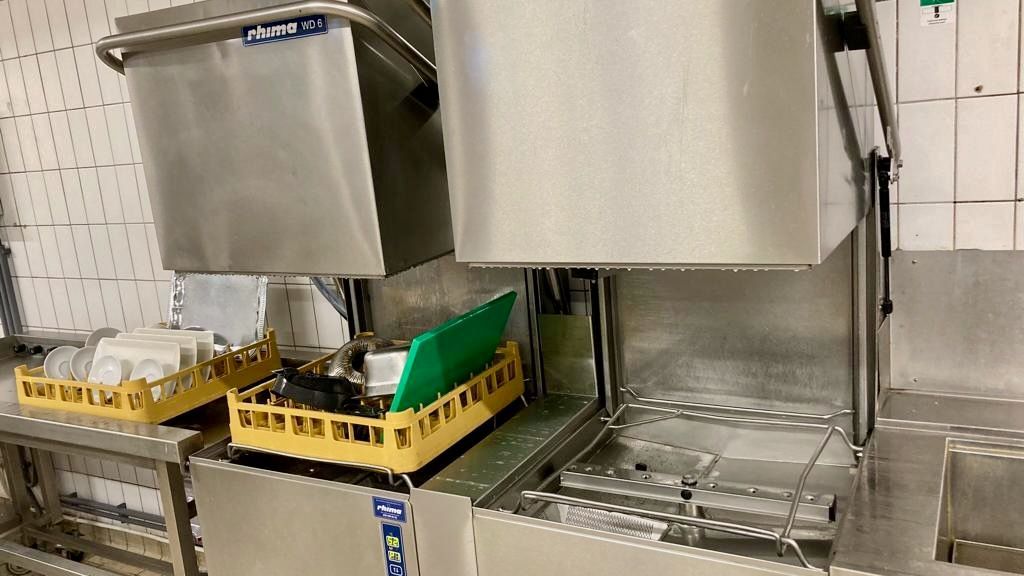 Gewerbliche Spülmaschine mit Tabletts für Geschirr und Besteck. Edelstahl in einer Küche.