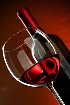 Vino tinto en copa, con una botella al fondo, sobre un degradado marrón.