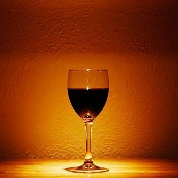 Copa de vino tinto sobre una superficie de madera, con un fondo de tonos cálidos.