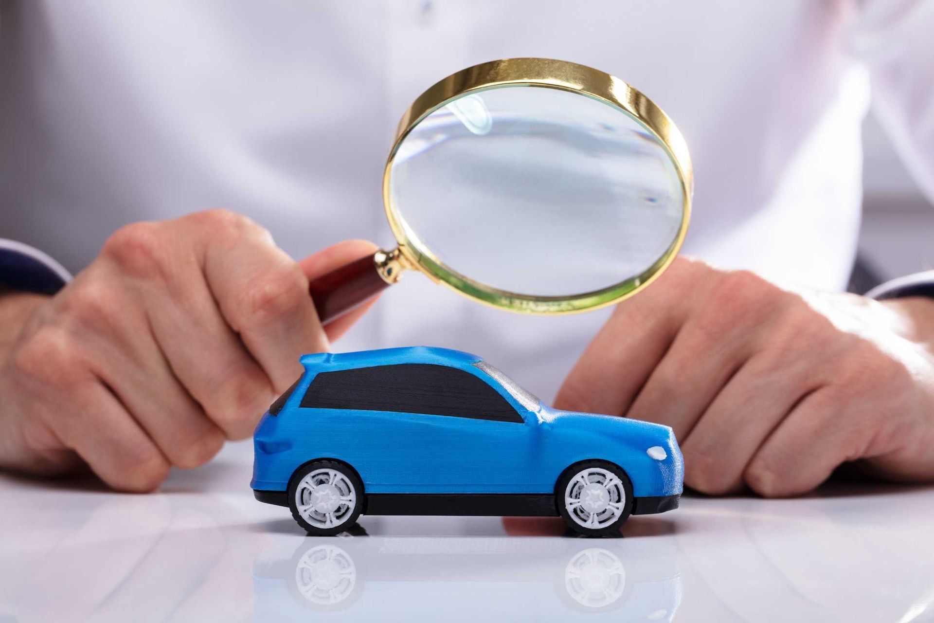 Una persona sostiene una lupa sobre un coche de juguete.