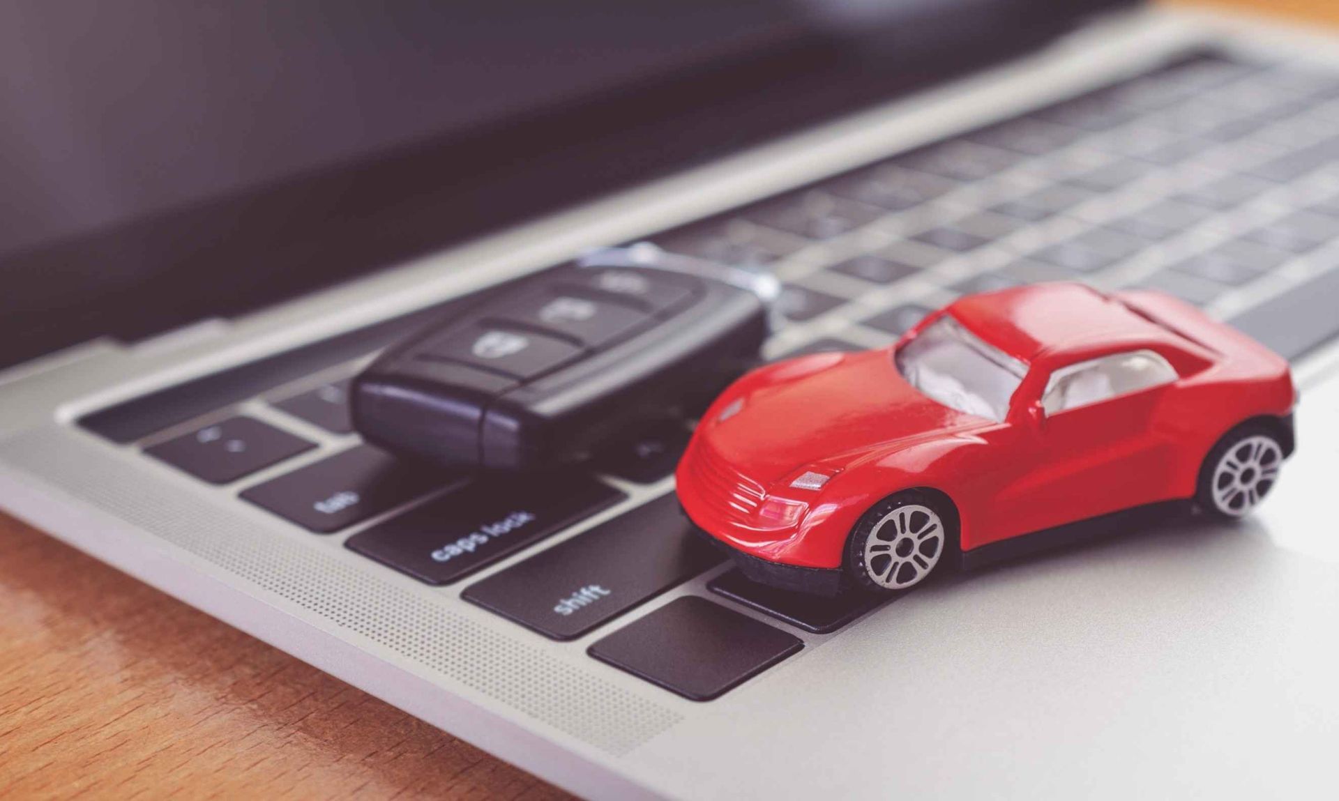Un coche de juguete rojo y una llave de coche están en un teclado de computadora portátil.