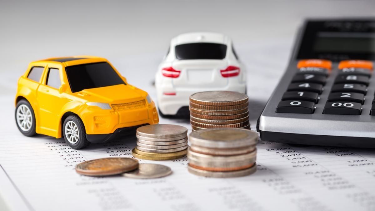 Hay dos coches de juguete junto a pilas de monedas y una calculadora.