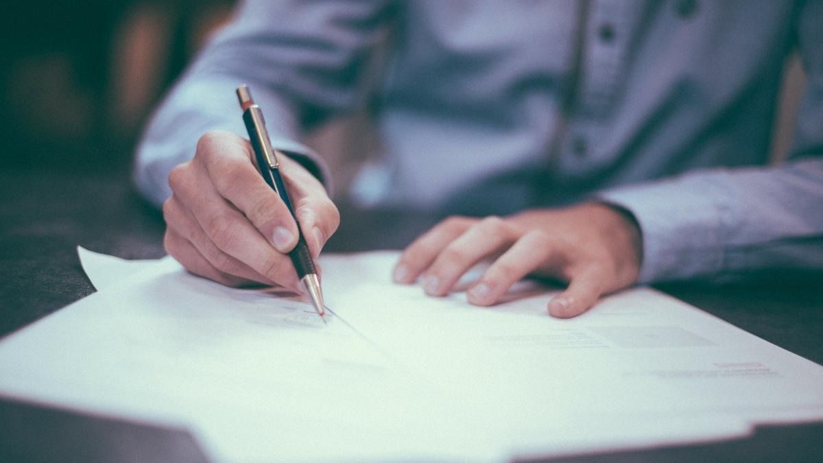 Un hombre está escribiendo en un trozo de papel con un bolígrafo.