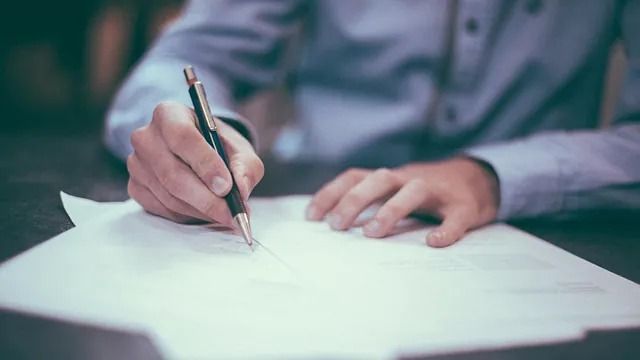 Un hombre está escribiendo en un trozo de papel con un bolígrafo.