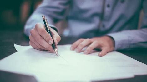 Un hombre está escribiendo en un trozo de papel con un bolígrafo.