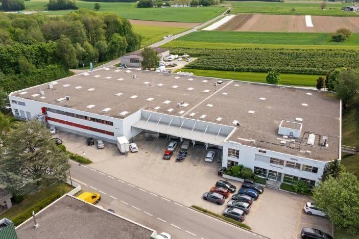 Vue aérienne d'un grand entrepôt entouré de camions, de voitures garées et de terres agricoles.