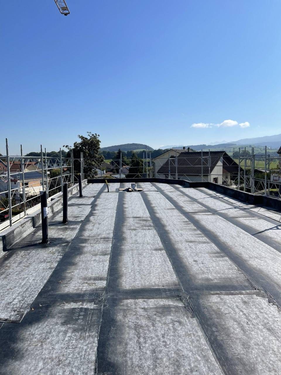Toit ensoleillé avec gravier blanc, balustrade et collines au loin sous un ciel bleu limpide