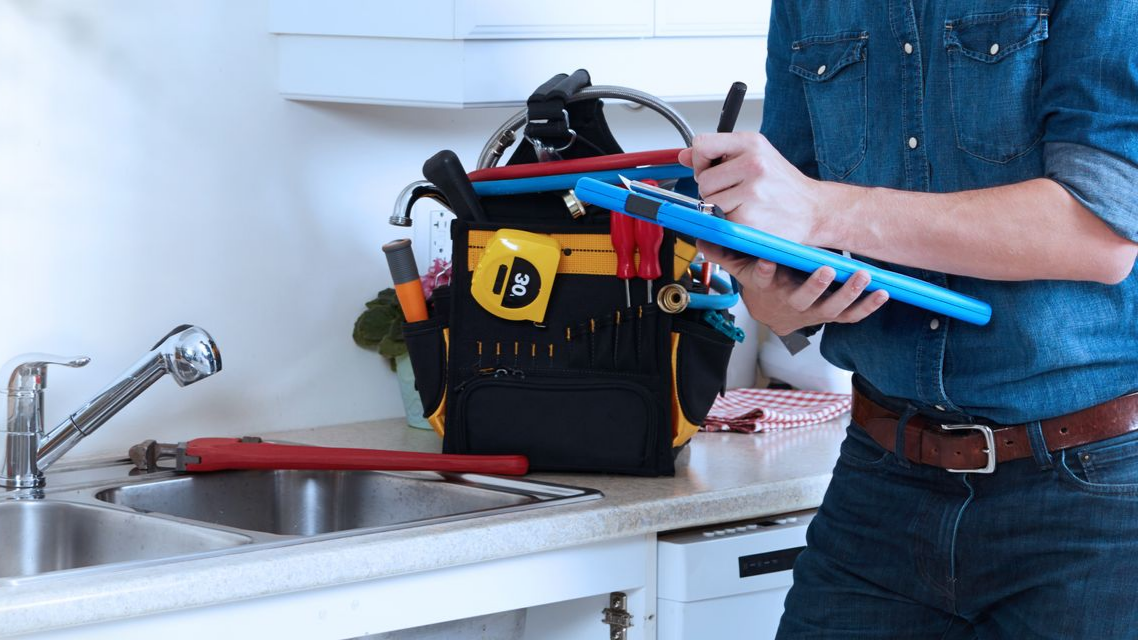 Une personne tenant une clé à pipe bleue au-dessus d'un évier avec une boîte à outils suggère une réparation de plomberie