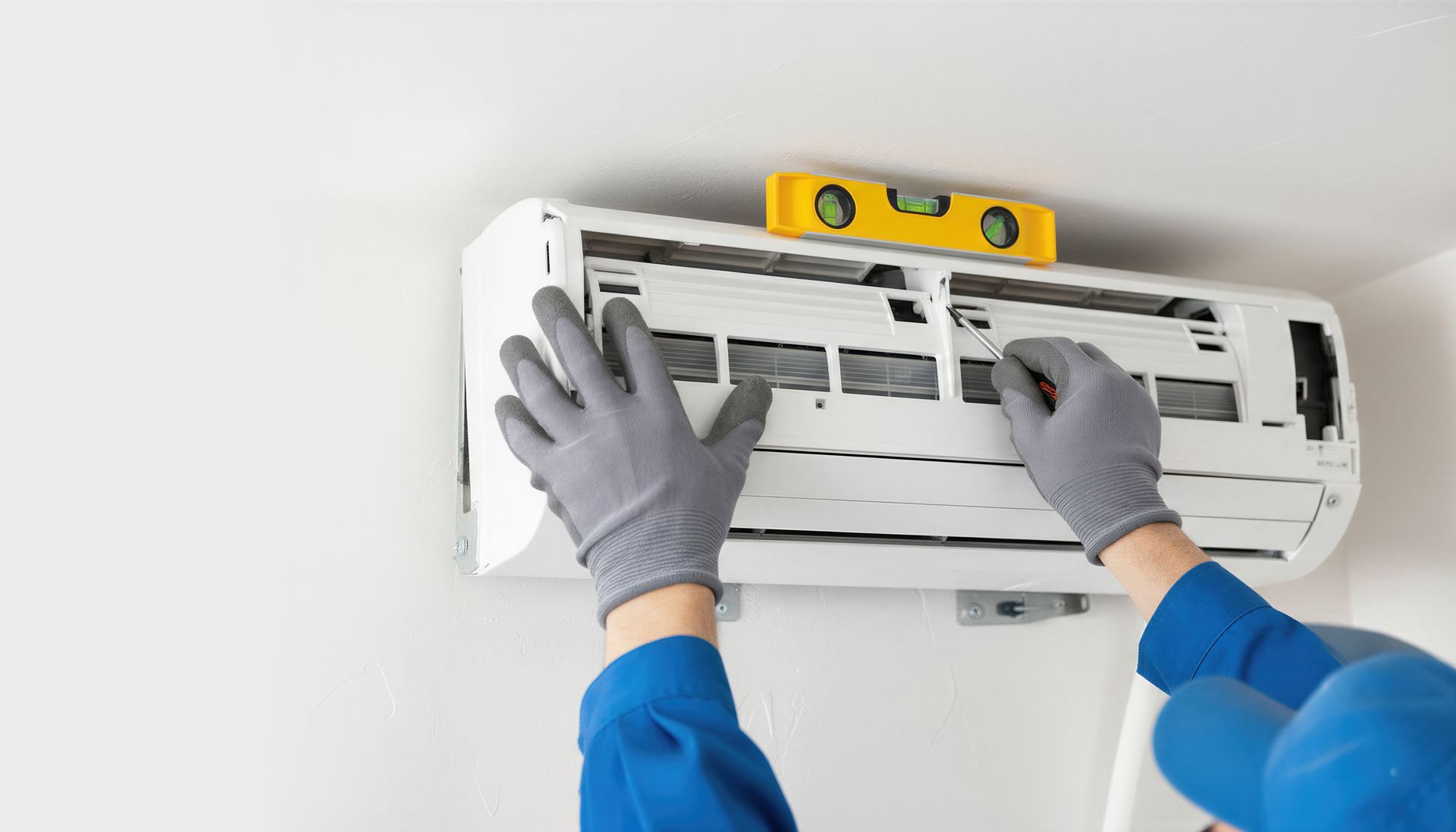 Des mains installent un climatiseur mural, en utilisant un niveau sur le bord supérieur.