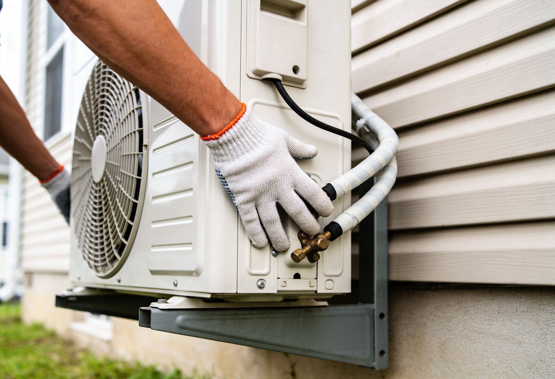Un technicien ganté raccorde un climatiseur contre un mur de maison