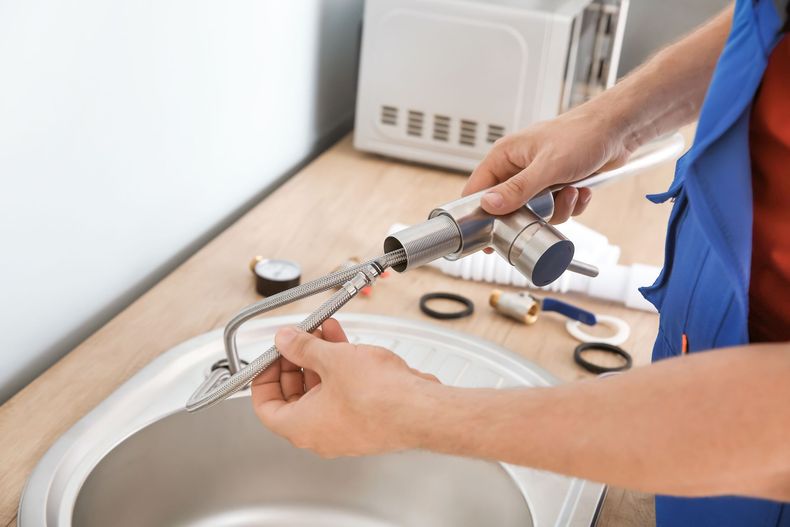 Une personne nettoie le bec d'un robinet d'évier de cuisine avec un chiffon et des outils.
