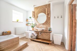 Salle de bains lumineuse avec meuble-lavabo en bois, miroir rond, parquet à chevrons et touches de blanc.