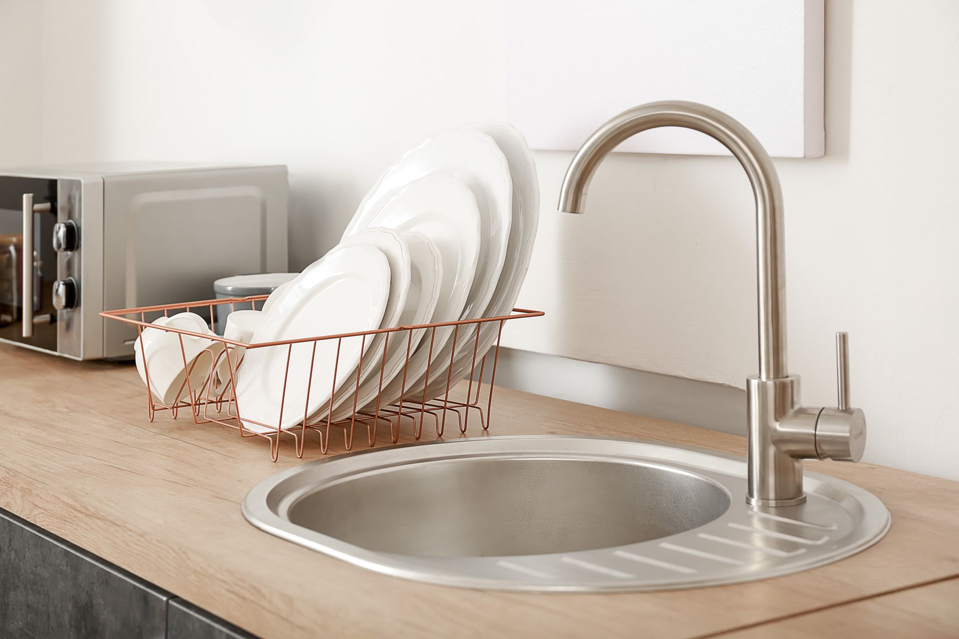 Évier de cuisine avec un égouttoir à vaisselle en assiettes blanches à côté d'un robinet sur un plan de travail en bois