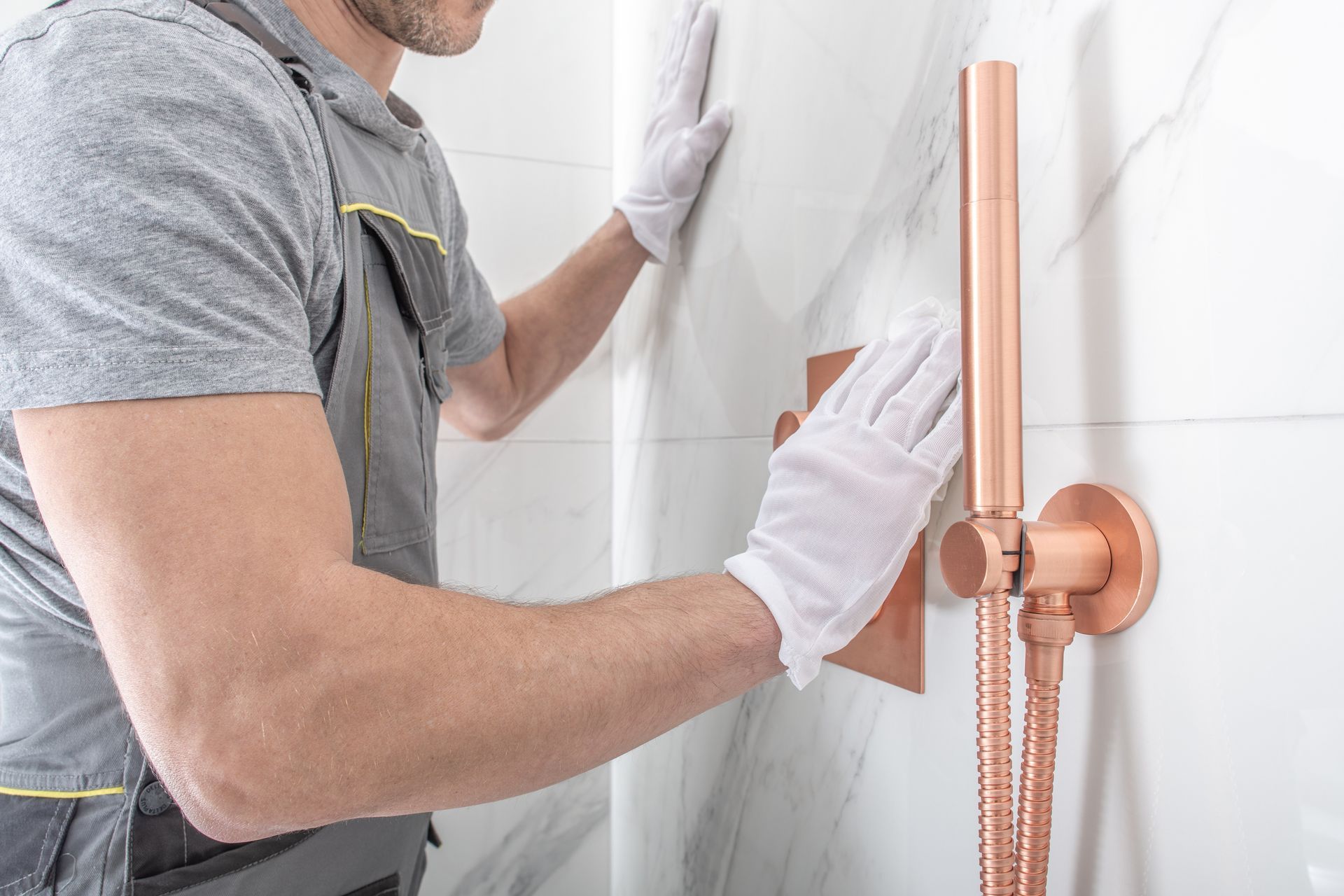 Ouvrier installant un robinet de douche en cuivre sur un mur de salle de bains carrelé