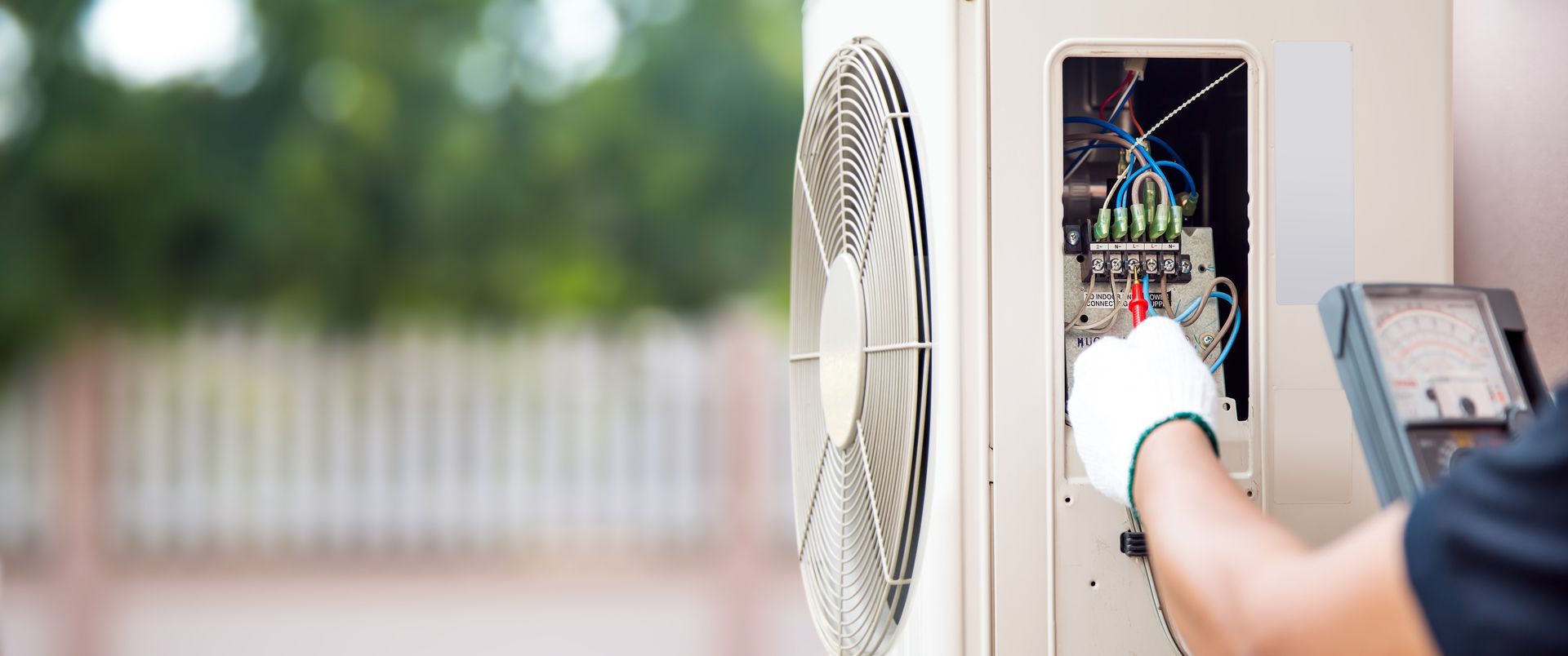 Un technicien vérifie une unité extérieure de climatiseur à l'aide d'un multimètre lors de la maintenance.
