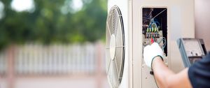 Un technicien vérifie une unité extérieure de climatiseur à l'aide d'un multimètre lors de la maintenance.