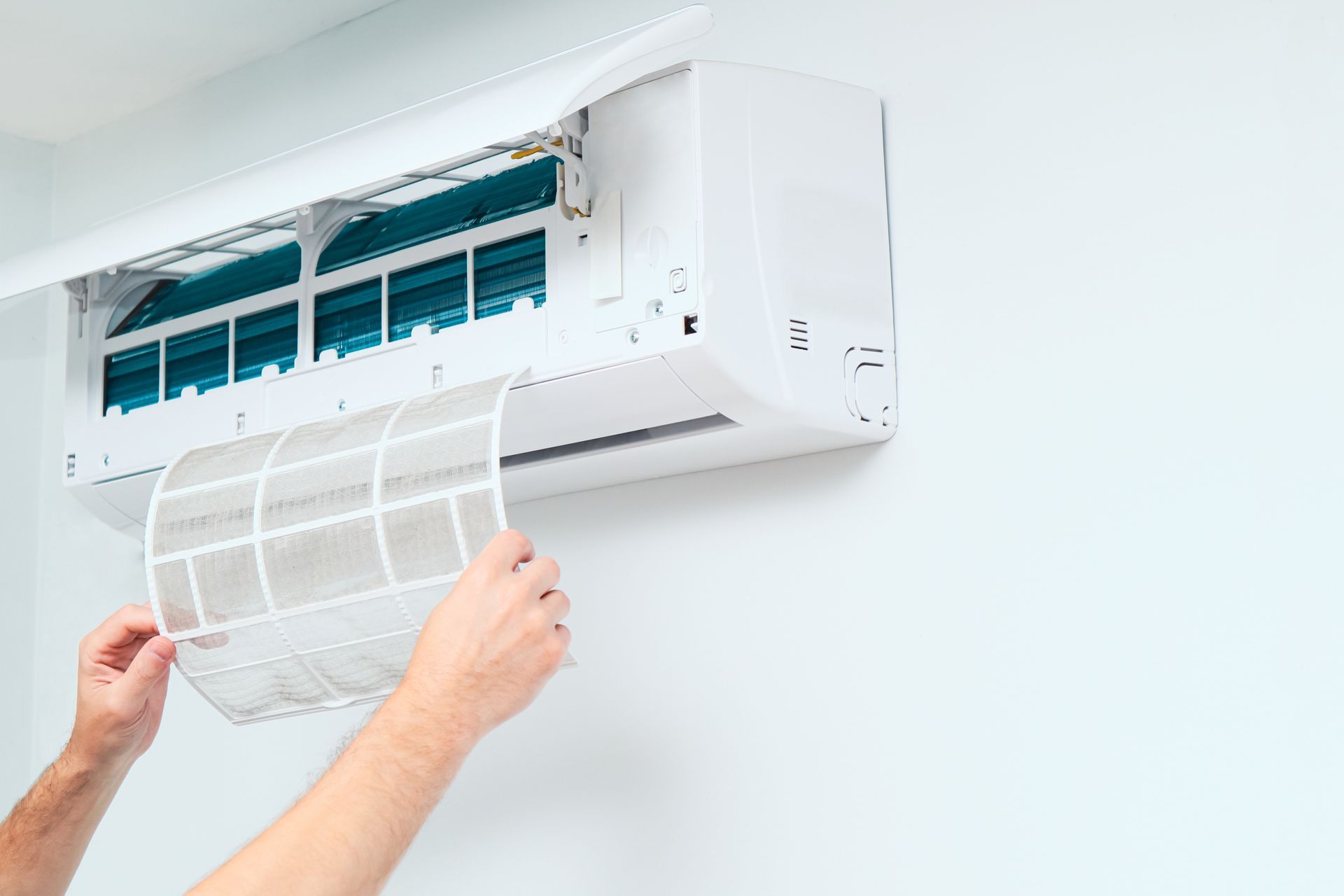 Mains retirant un filtre sale d'un climatiseur mural blanc