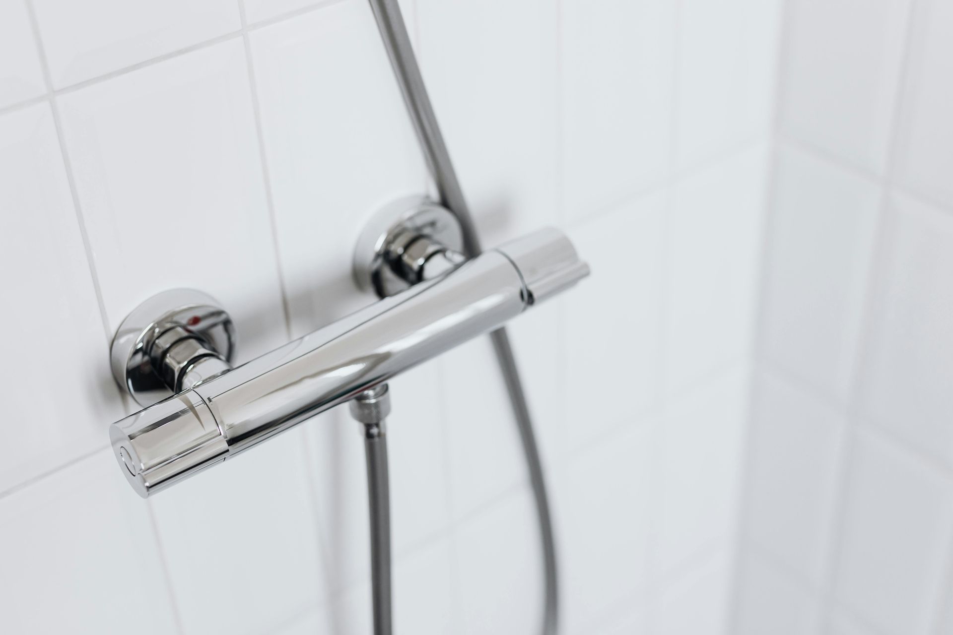 Mitigeur de douche chromé avec flexible, sur fond de carrelage blanc.