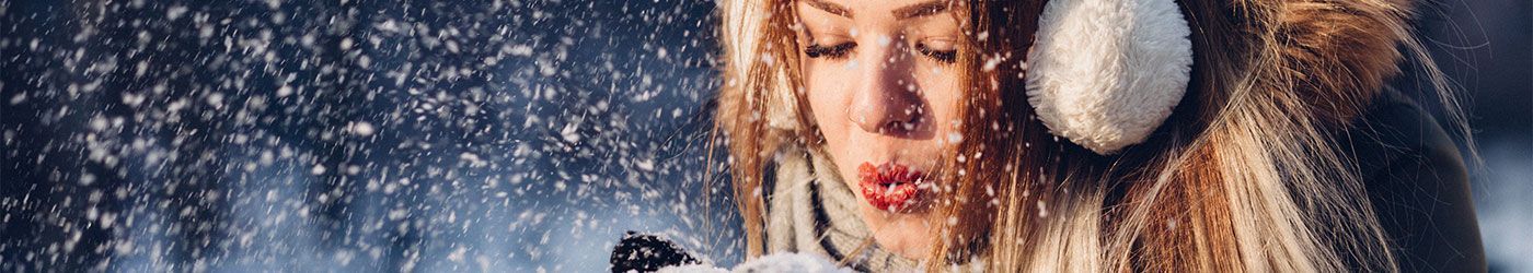 Eine Frau mit Ohrenschützern bläst Schnee in die Luft.