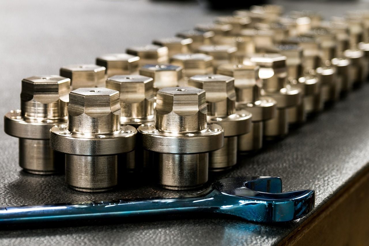 Fila de sujetadores metálicos con cabezas hexagonales sobre una mesa, una llave inglesa azul en primer plano.