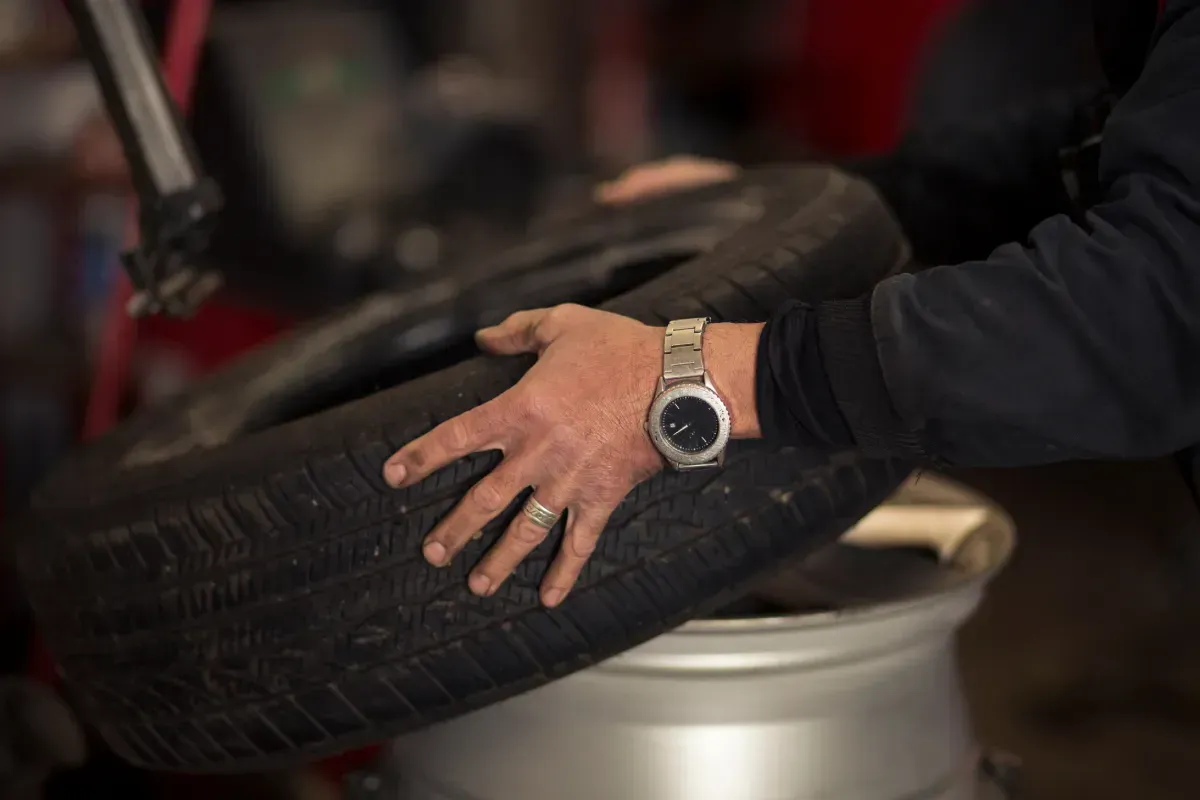 Manos sosteniendo un neumático cerca de una llanta plateada en una tienda.