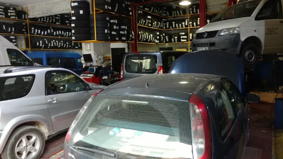 Interior de taller de reparación de automóviles con vehículos, neumáticos y equipos.