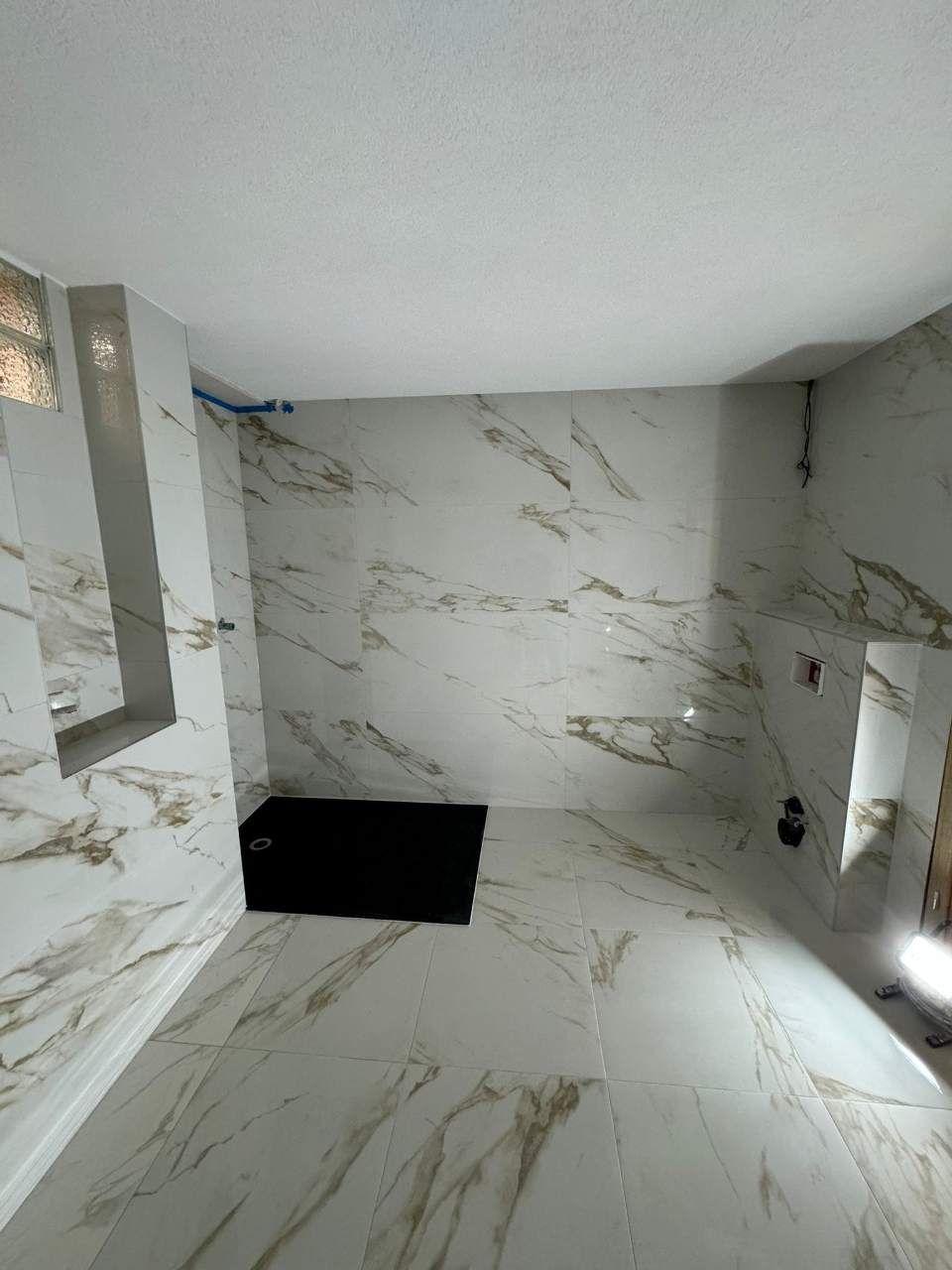 Salle de bains carrelée de marbre blanc veiné de doré. Caisson noir au sol. Étagères encastrées, robinetterie.