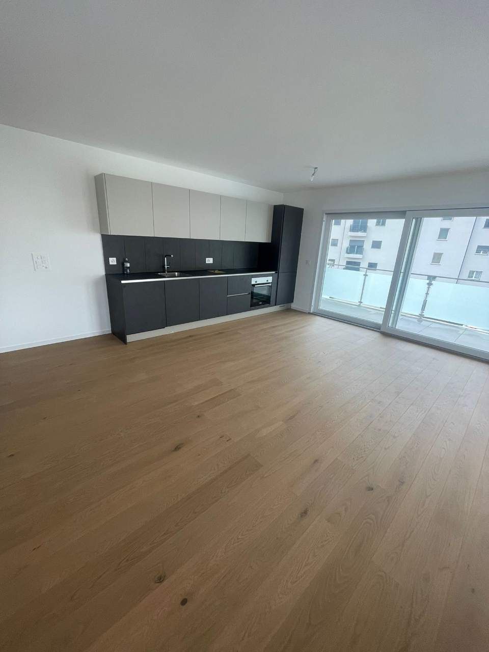 Cuisine moderne vide avec placards gris foncé et beige clair, parquet et grandes portes coulissantes.