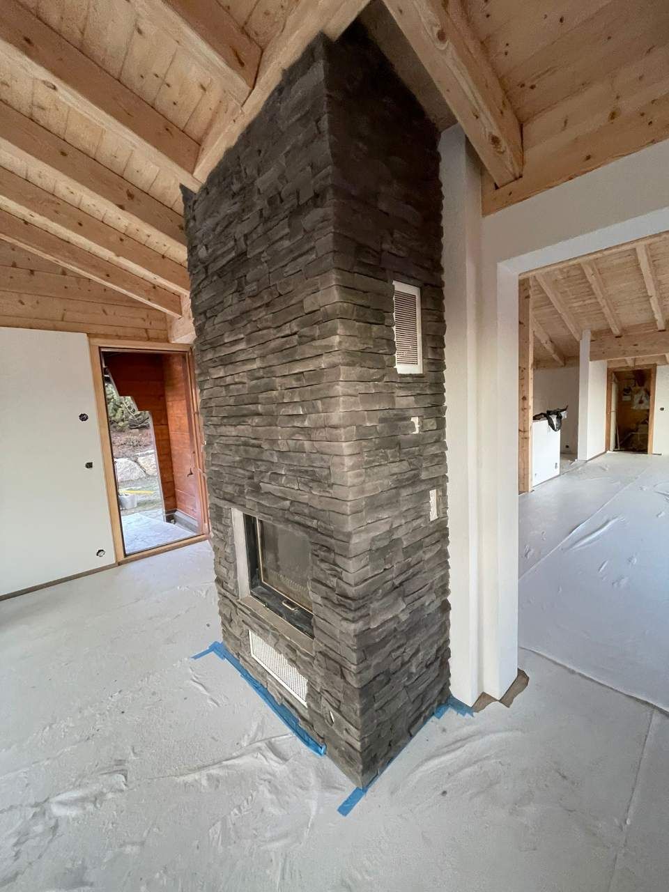 Cheminée revêtue de pierre dans une pièce au plafond en bois clair et aux murs blancs.