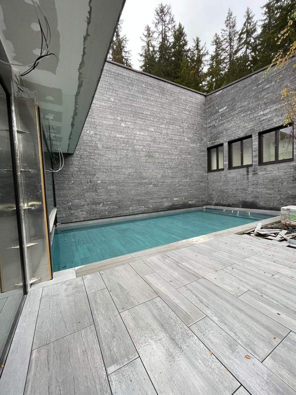 Vue extérieure d'une petite piscine rectangulaire entourée de murs en pierre grise et d'une terrasse en bois.