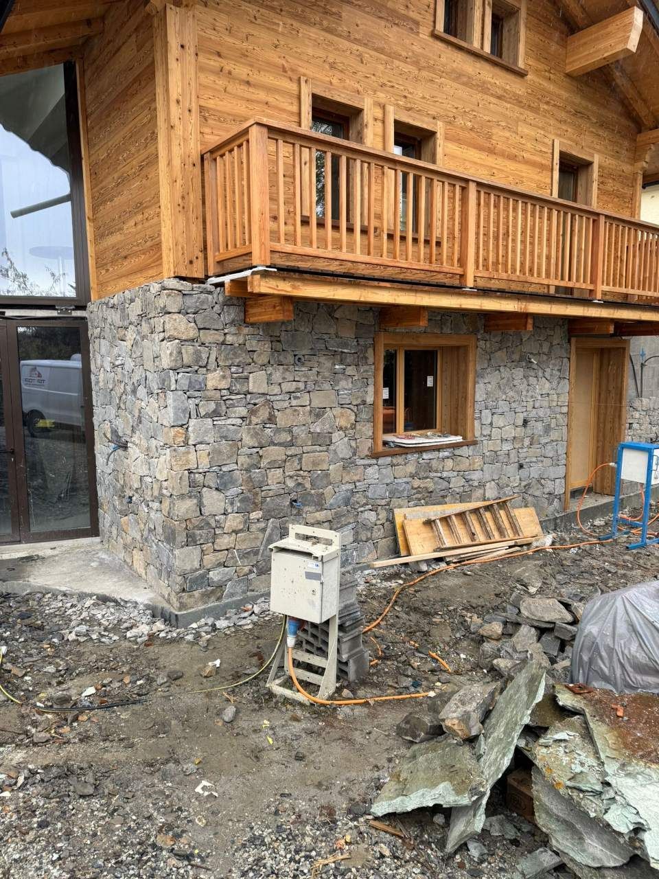 Extérieur d'un bâtiment avec façade en pierre, étage supérieur en bois et balcon, chantier de construction au premier plan.
